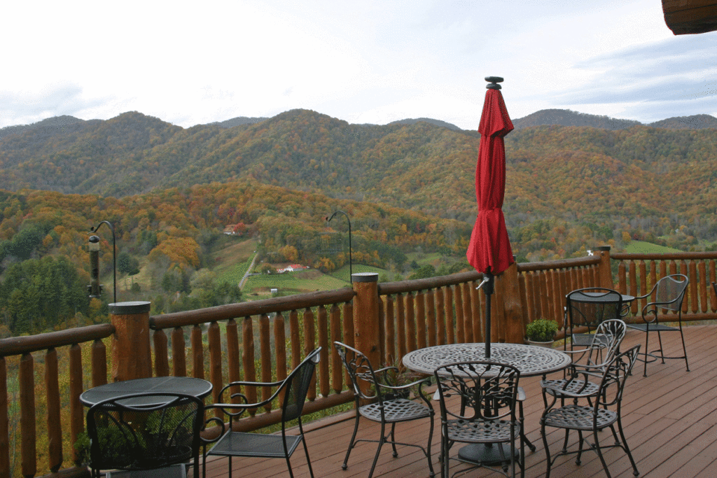 Deck with red umbrella and bistro tables and chairs. Distant mountains and fog spot lighting the fall foliage in the valley of Rocky Mountains