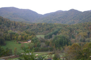 Mountain views with yellow, orange, red and green leaves. Countryside and homes in the foreground.