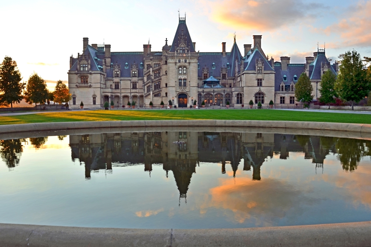 Biltmore Estate with reflecting pond in front, blue sky with one big orange-tinged cloud as background