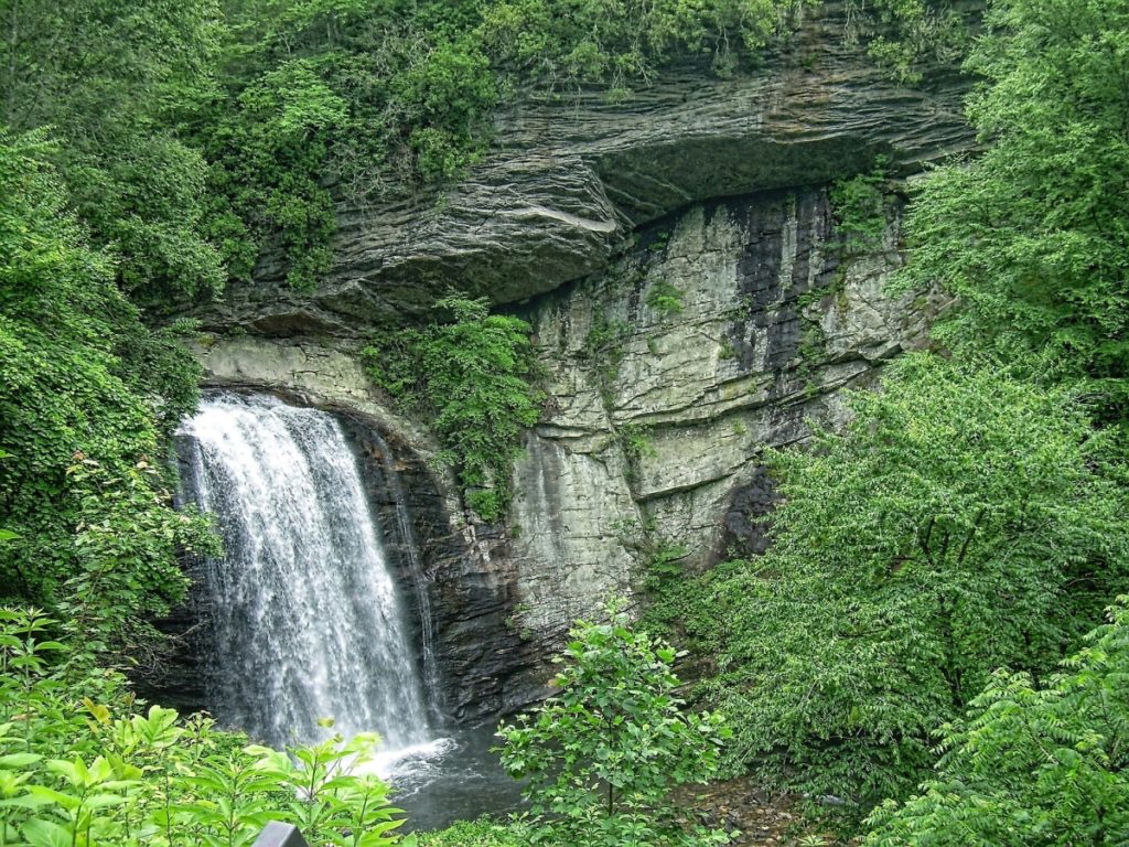 Looking Glass Waterfall in lower left quadrant, justing from rocky cliff, surrounded by green trees
