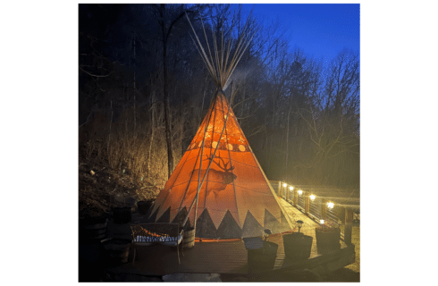 A glowing Native American TiPi with a dark sky backdrop looks inviting