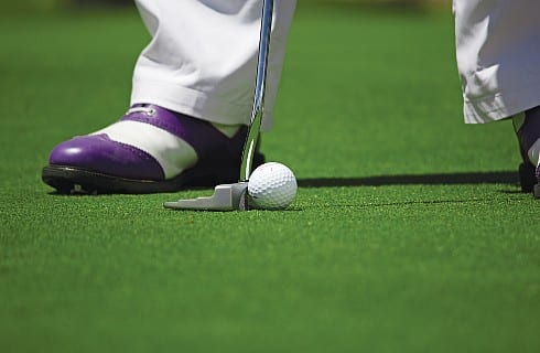 Legs of golfer with white pants and brown and white shoes with putter on green