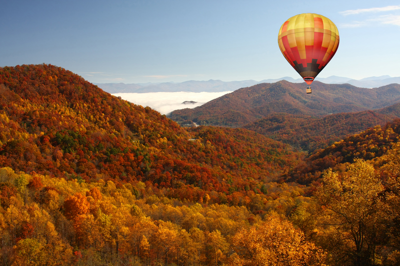 a yellow, orange, and brown hot air balloon flying over the smokey mountains and trees the same colors 