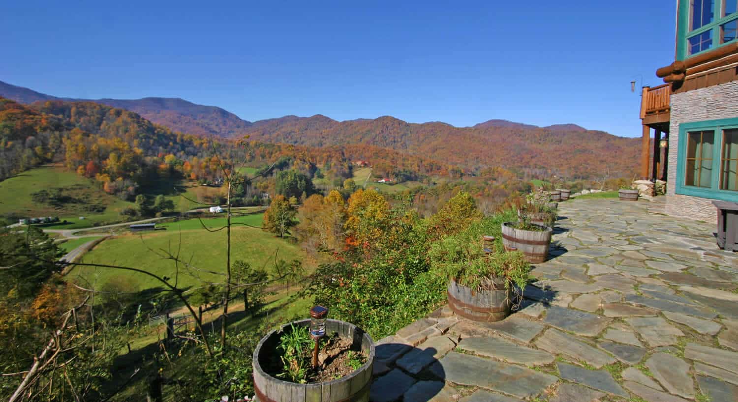 Stone patio overlooks a green valley and extended hills covered in fall foliage.