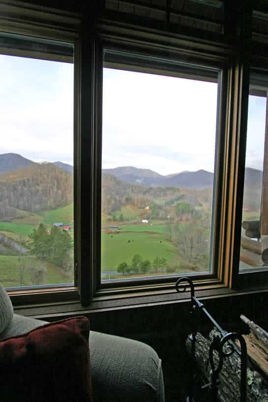 View of a green vallley from outside a window next to a cozy chair. 