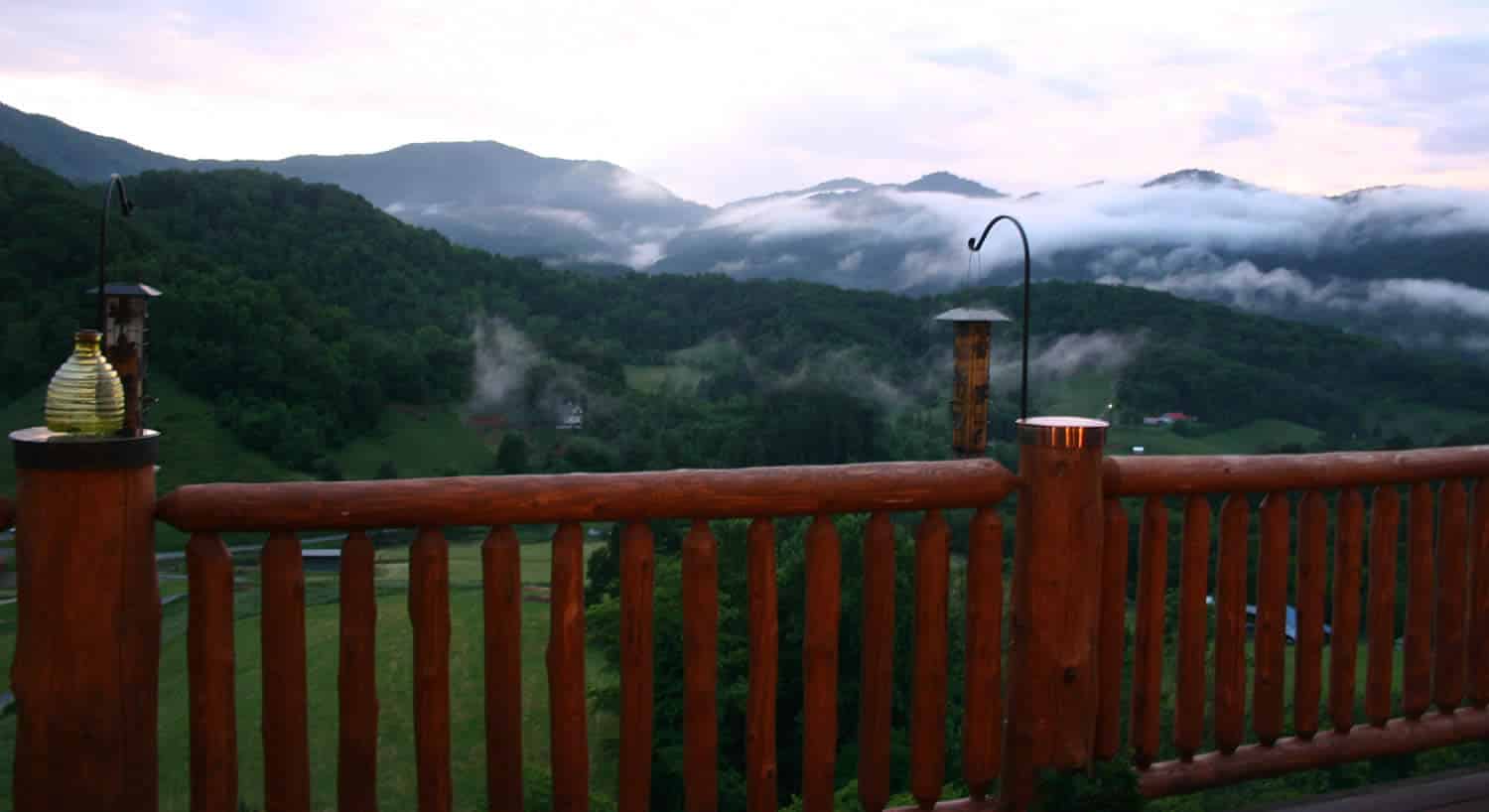 View of misty mountains and a green valley from a wooden deck with bird feeders.