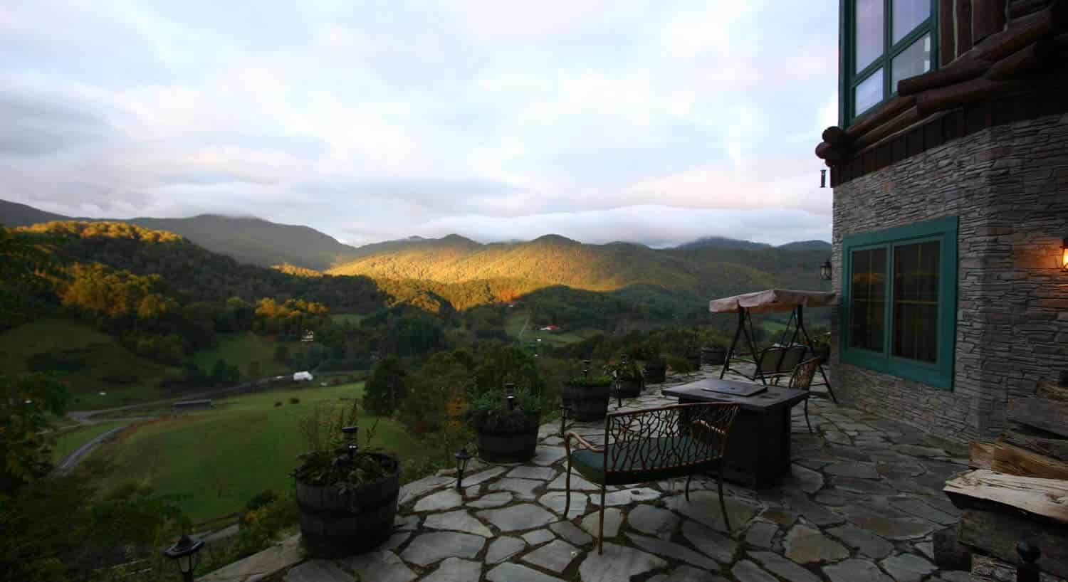 Stone patio of large home overlooking the green valley below. 