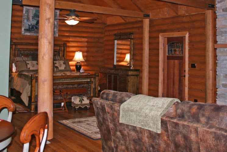 Large suite with wooden bed, log-cabin walls, a stone fireplace, leather sofa and table and chairs.