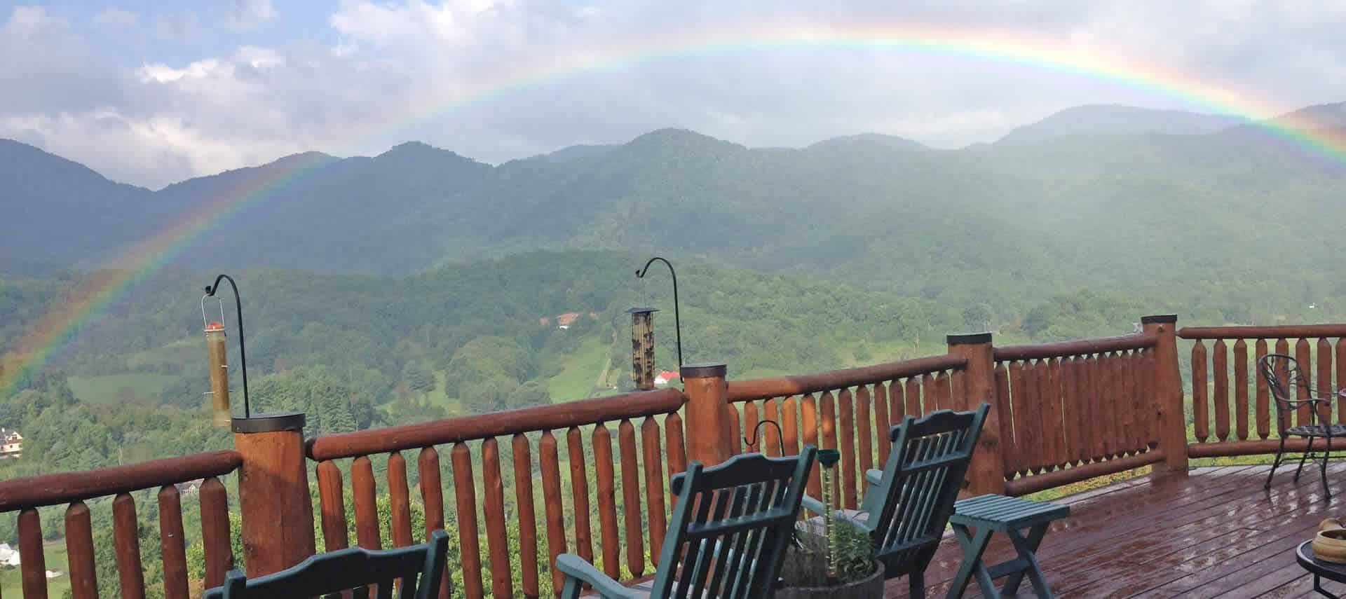 Beautiful rainbow seen through the mist from a wooden deck with green patio chairs. 
