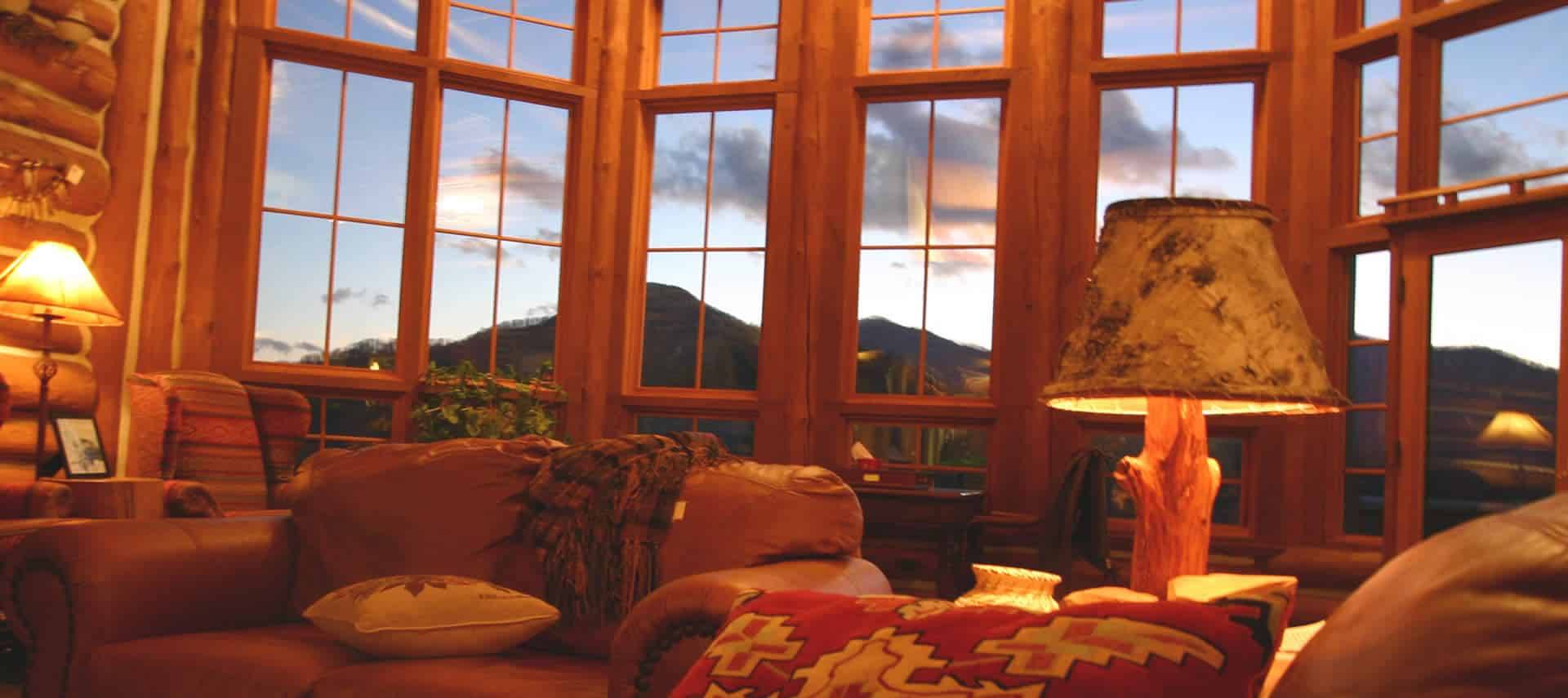 Warm interior living space with leather furniture looks out windows to mountains. 