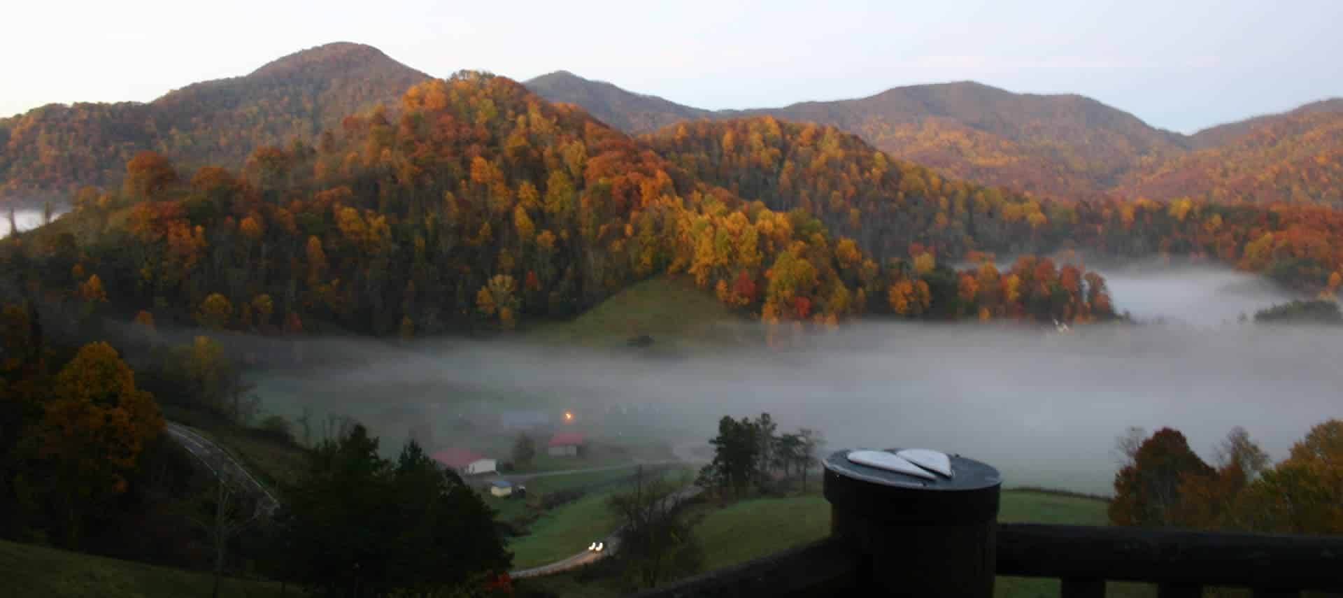 Mountain valley covered by mist, surrounded by trees and hills bursting with fall foliage. 