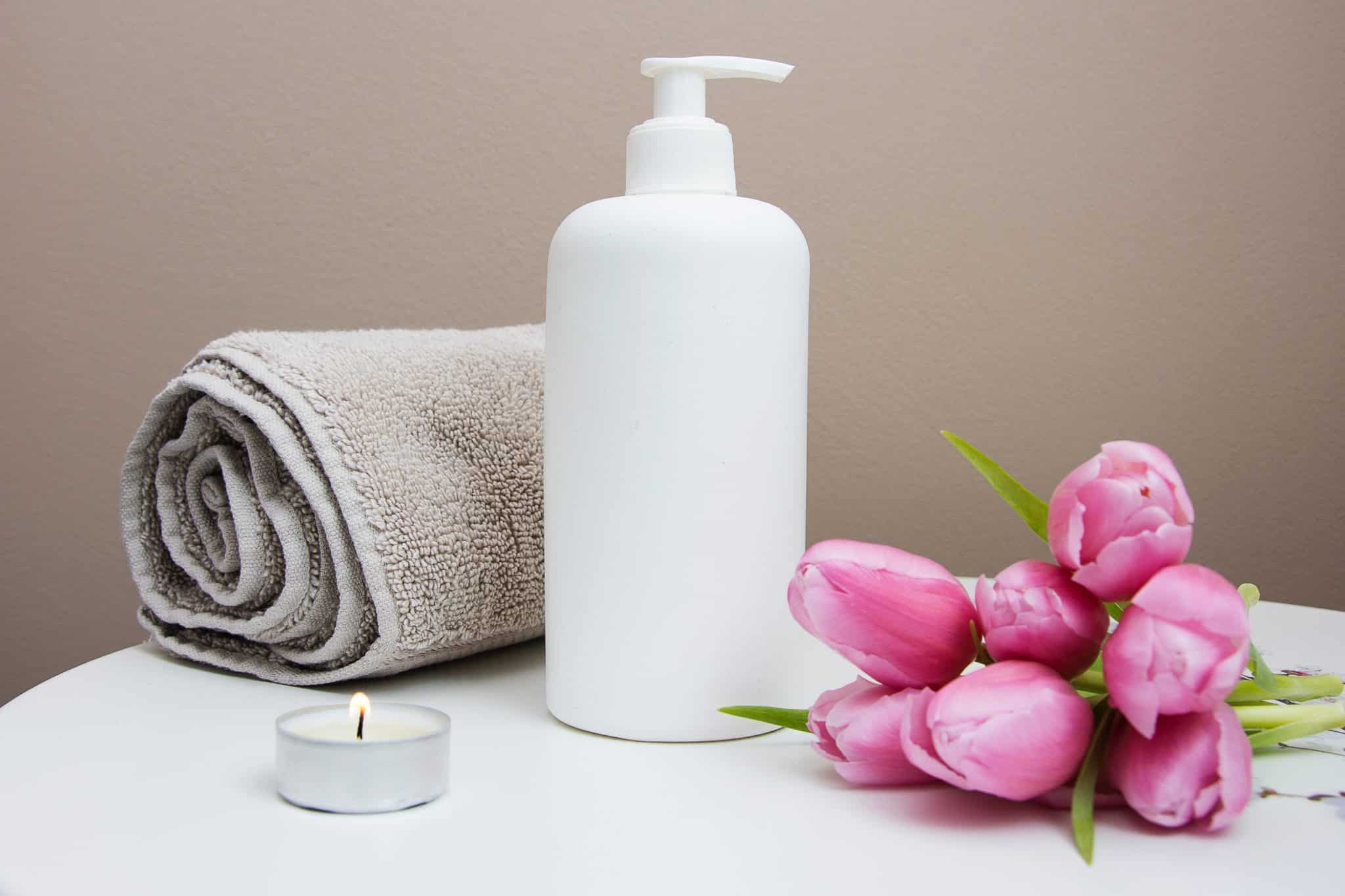 Spa table with rolled towel, lotion, candle and flower