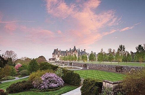 Wide angle view of the sprawling green grounds with manicured shrubs and flowers with large caslte in background and blue sky with clouds and pink sunset