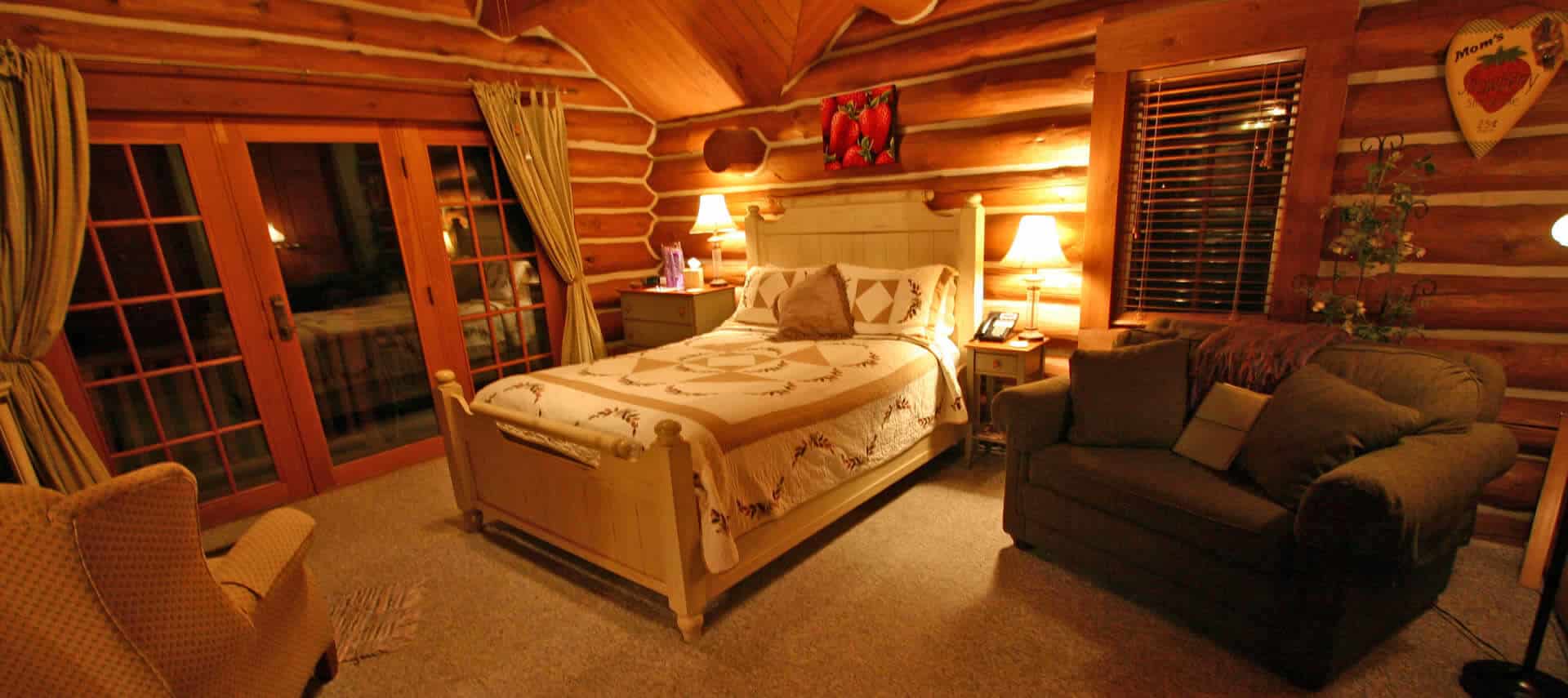 Warm bedroom in a log-cabin setting with a quilt-covered bed, a sofa and wingback chair.