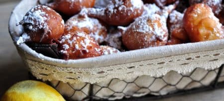 Wire basket lined with white cotton filled with apple fritters dusted with confectioners sugar.