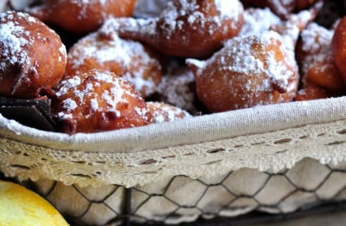 Wire basket lined with white cotton filled with apple fritters dusted with confectioners sugar.