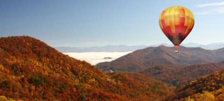 Hot air balloon drifting over fall foliage in mountains