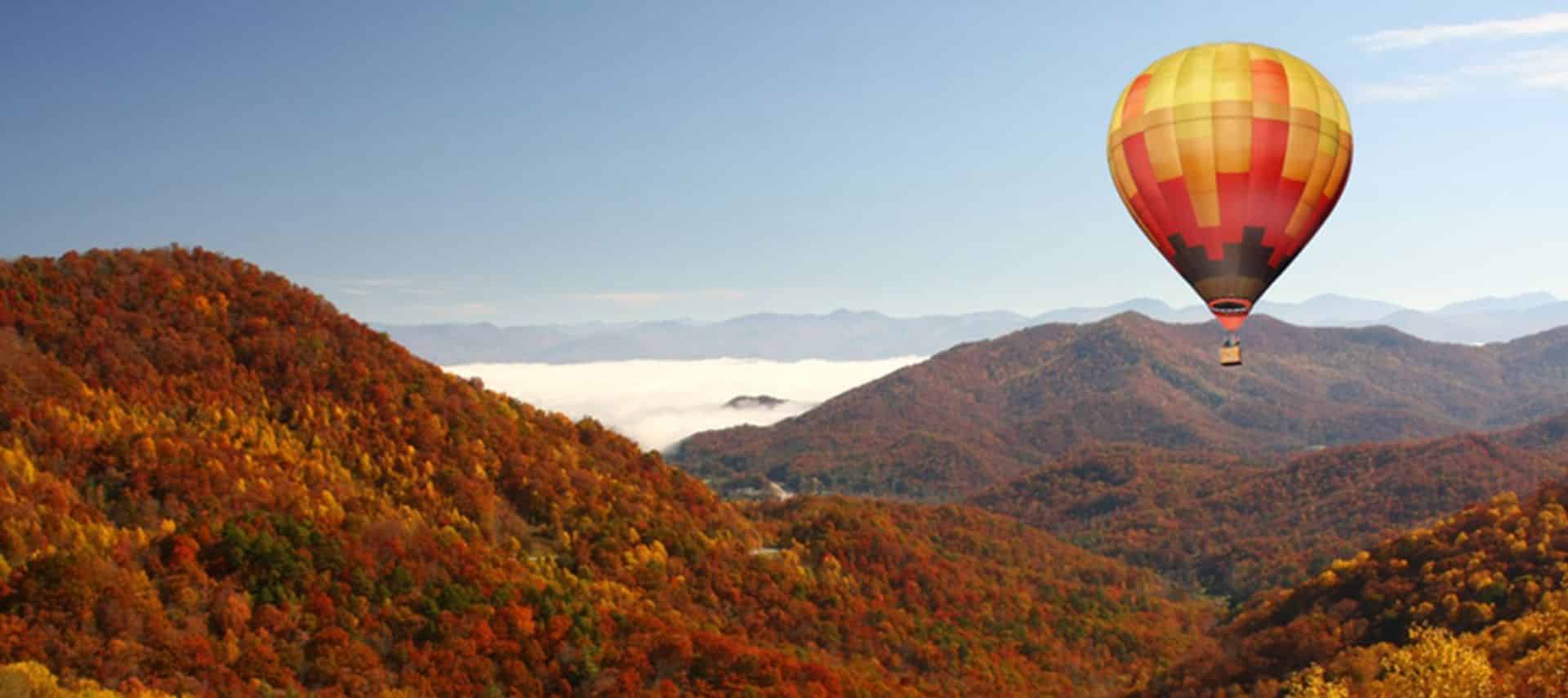 Hot air balloon drifting over fall foliage in mountains