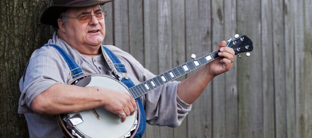 a man singing and playing banjo outside by a tree