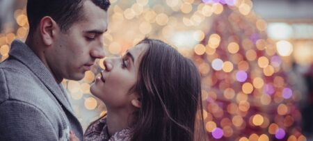 young couple bracing for a kiss outdoors with holiday lights blurred in the background
