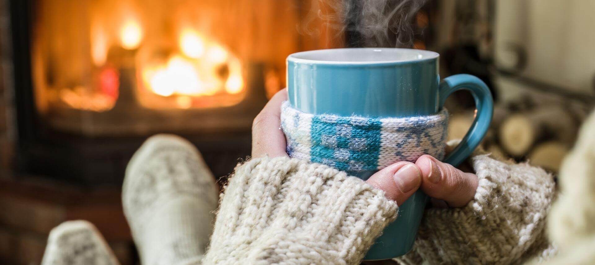 Woman holding mug and sitting by a cozy fireplace.