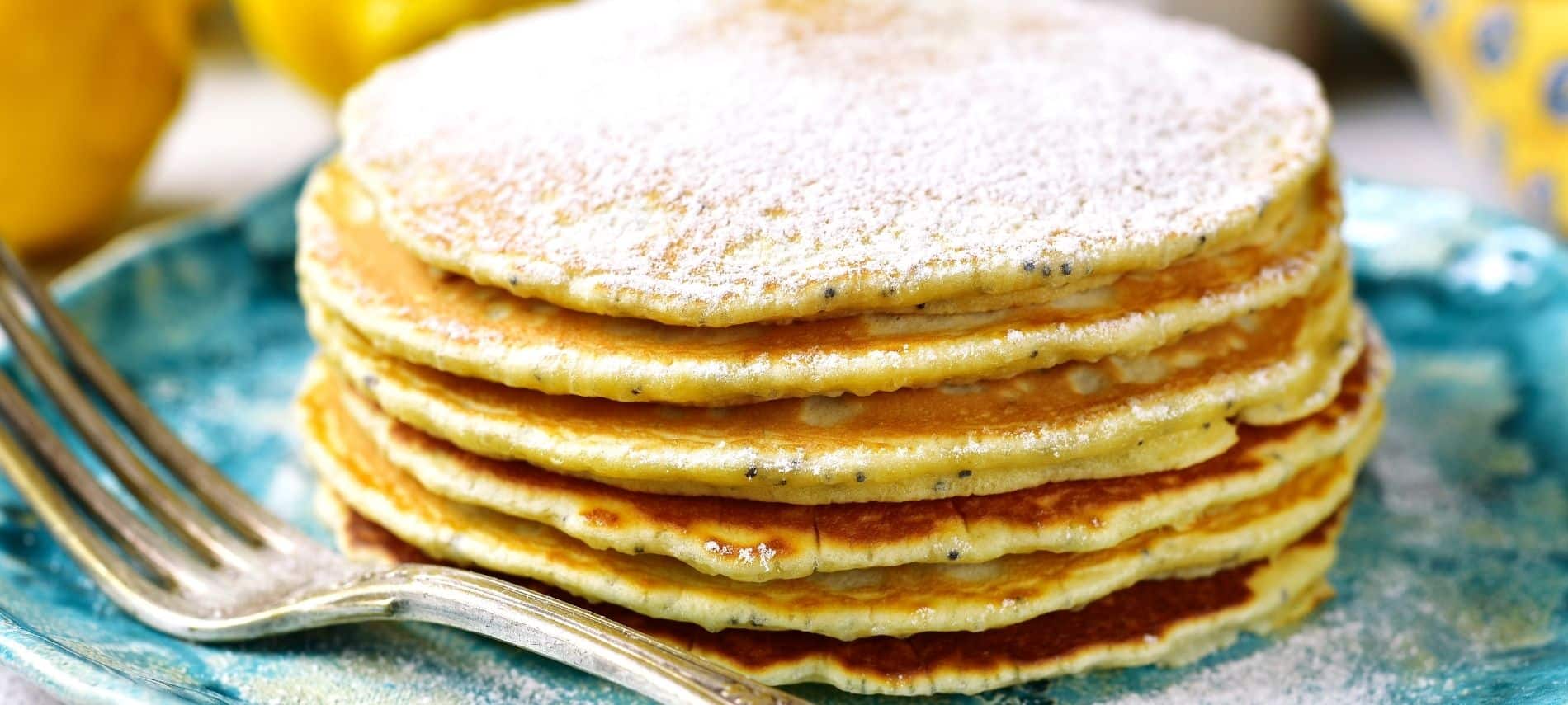 Blue plate topped with a stack of lemon pancakes dusted with powdered sugar