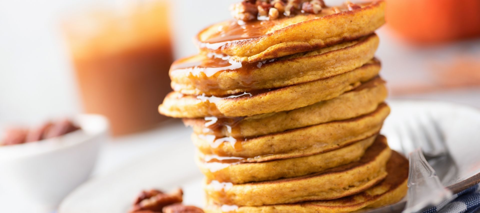 Stack of pecan pancakes with syrup, pecans on top with glass of juice behind