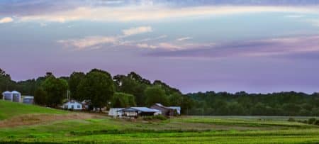 Purple and blue sky over fields and farmhouse