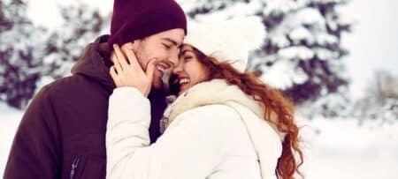 a romantic couple embracing with snowy trees behind them