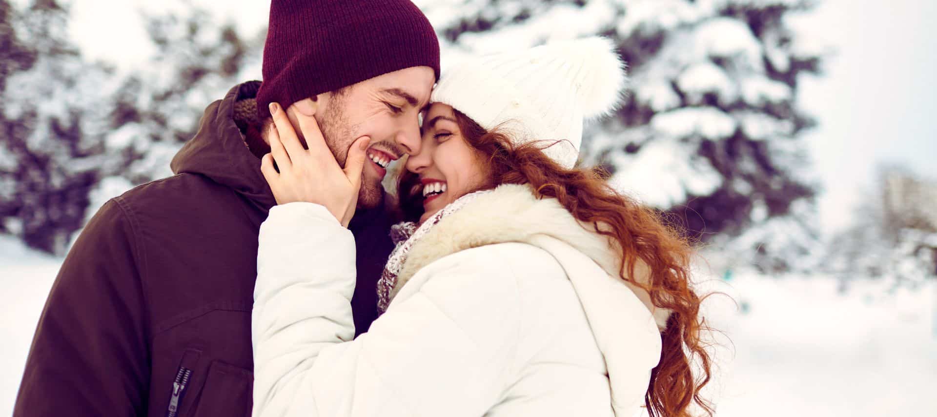 a romantic couple embracing with snowy trees behind them