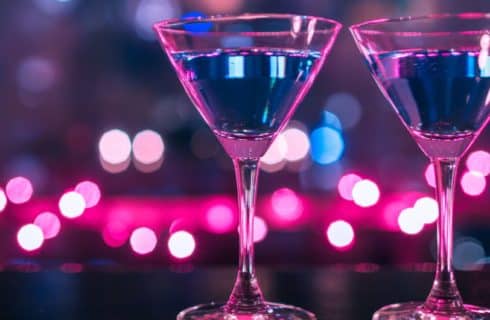 Glasses of clear liquid with sparkling blue and pink colored lights around them.