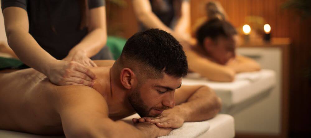 couple receiving a side by side massage with the man in the foreground and a blurred woman and candles in the backdrop