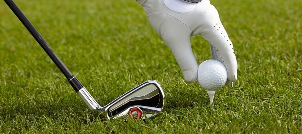 closeup of person with golf glove placing golf ball on tee and club on the side