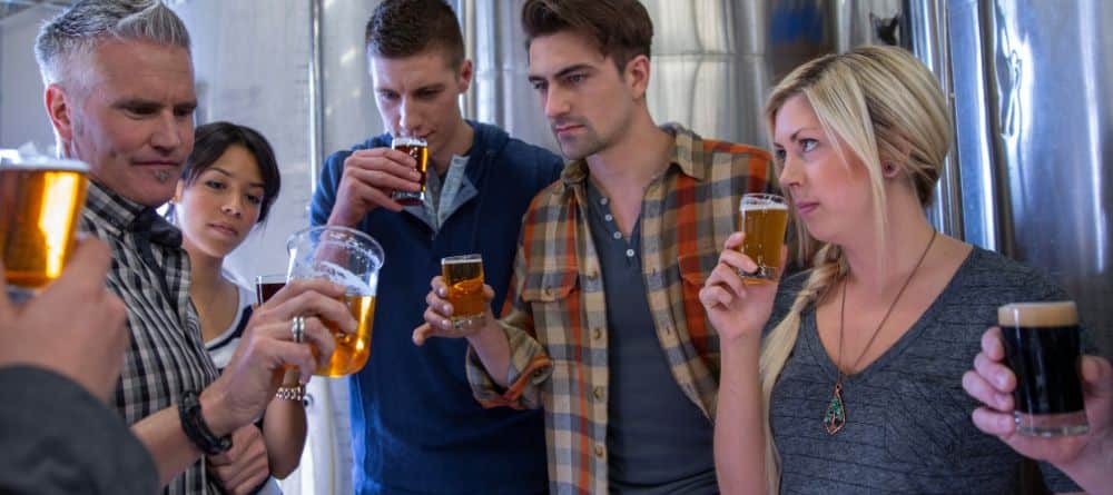 People standing near tanks of beer are sampling a glass of beer. 