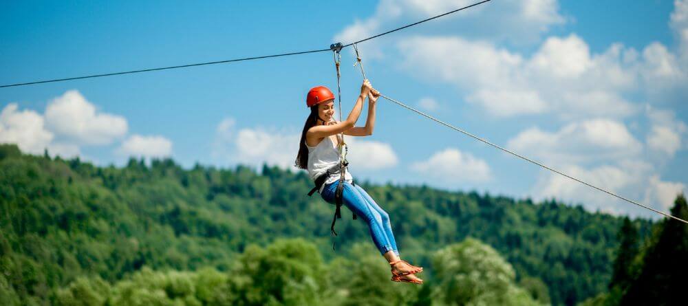 woman wearing a helmet and riding a zipline over open air and tree canopies
