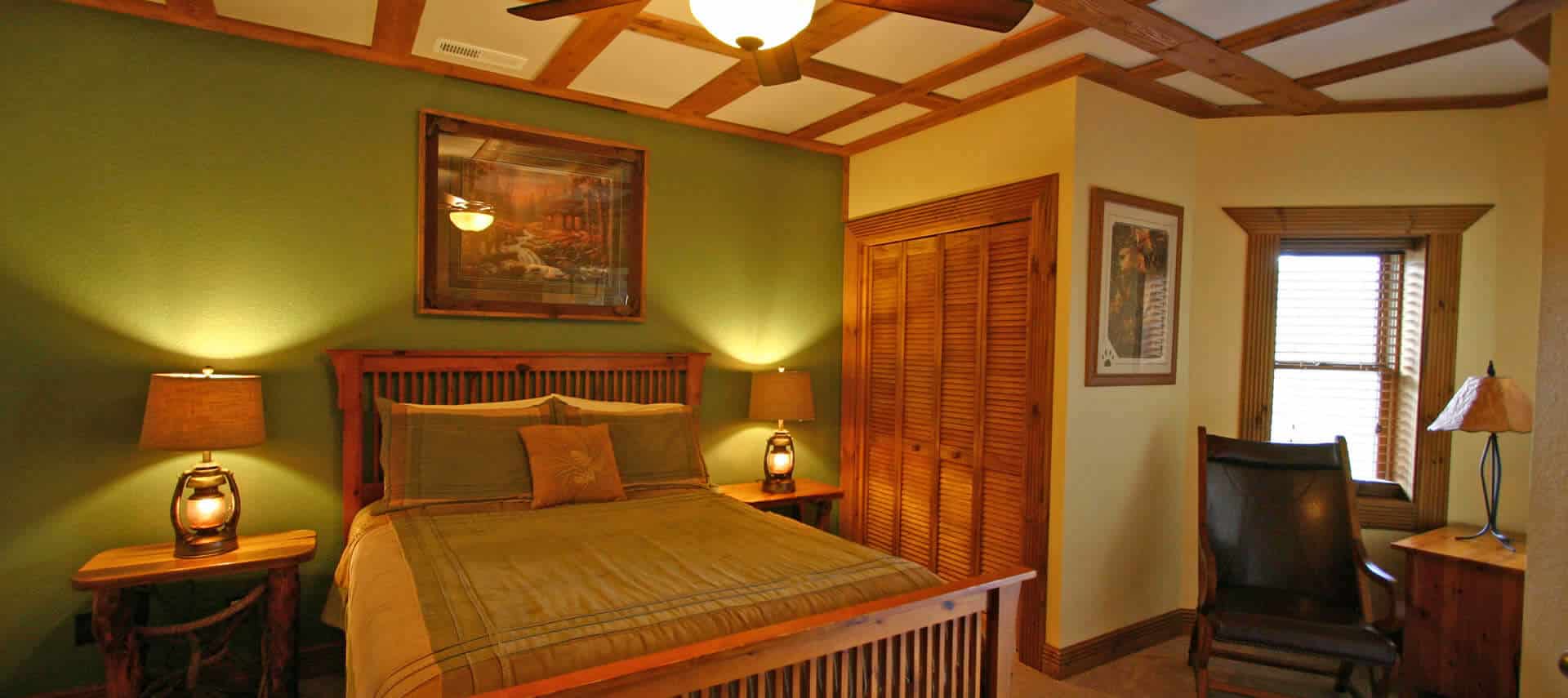 Large bedroom in green and cream with wooden accents, bed, nighstand and chair.
