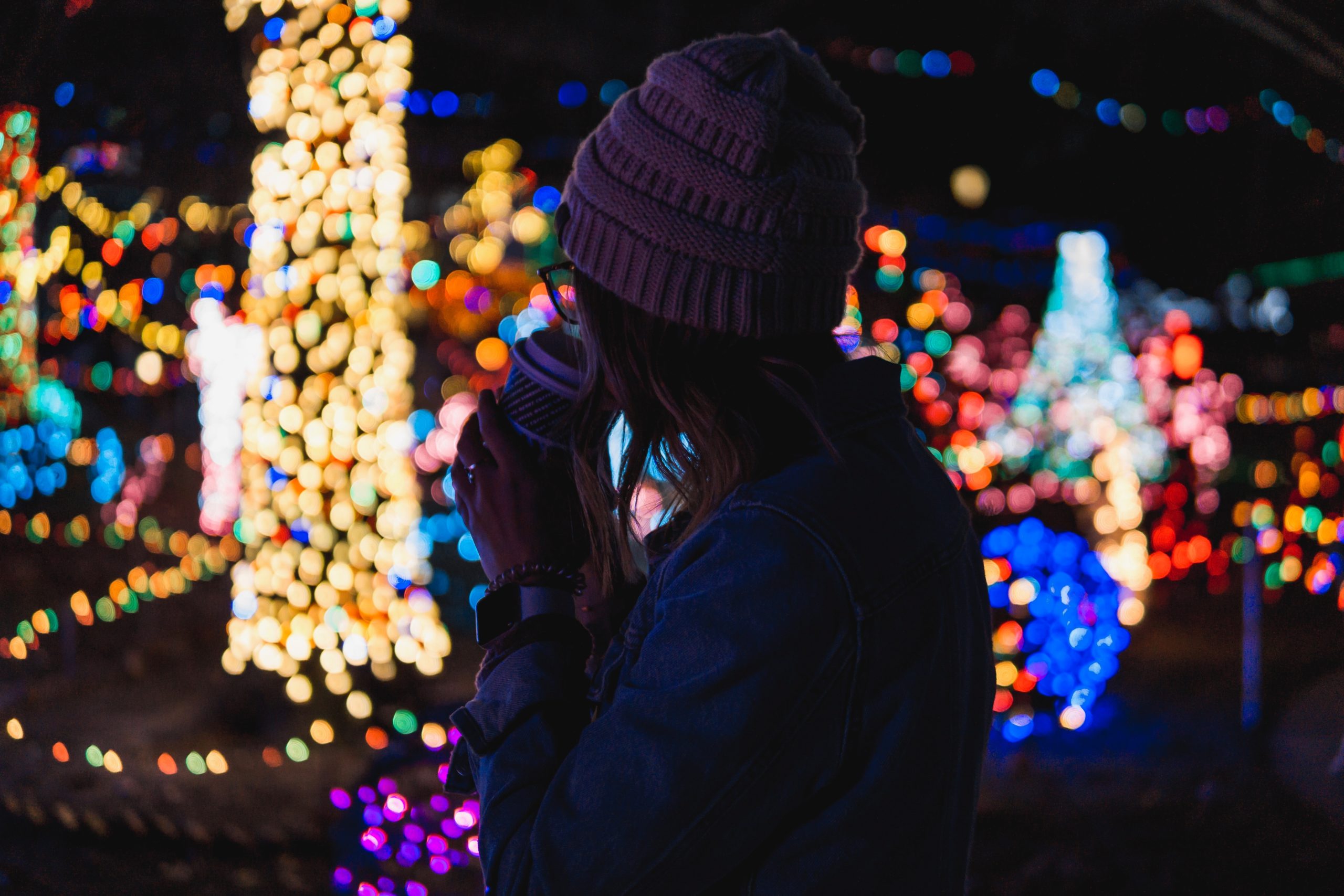 A woman sipping hot chocolate in a field of multicolor holiday lights.